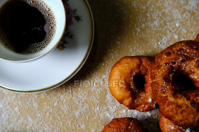 Vue de dessus des beignets délicieux avec sucre en poudre et des tasses de thé chaud placées sur la table à la maison — Photo de stock