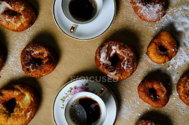 Vista dall'alto di deliziose ciambelle con zucchero a velo e tazze di tè caldo poste sul tavolo a casa — Foto stock