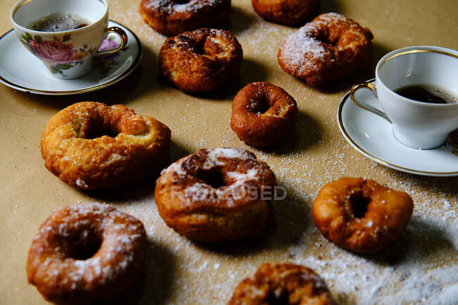 Vista superior de deliciosos donuts com açúcar em pó e xícaras de chá quente colocadas na mesa em casa — Fotografia de Stock