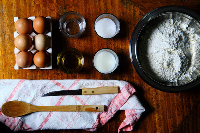 Vista superior de varios ingredientes frescos para la preparación de pasteles colocados cerca de la servilleta con utensilios en la mesa de madera en la cocina - foto de stock
