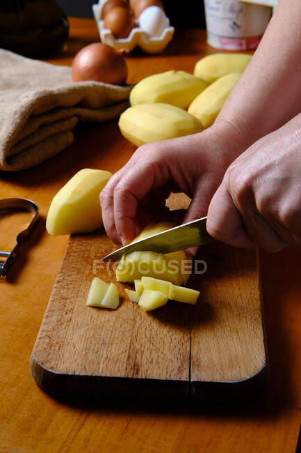 Cultivar anônimo cozinhar descascando batata acima da placa de corte de madeira na cozinha moderna — Fotografia de Stock