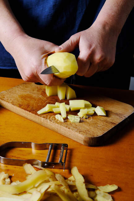 Обрізати анонімний кухар чистку картоплі над дерев'яною обробною дошкою на сучасній кухні — стокове фото