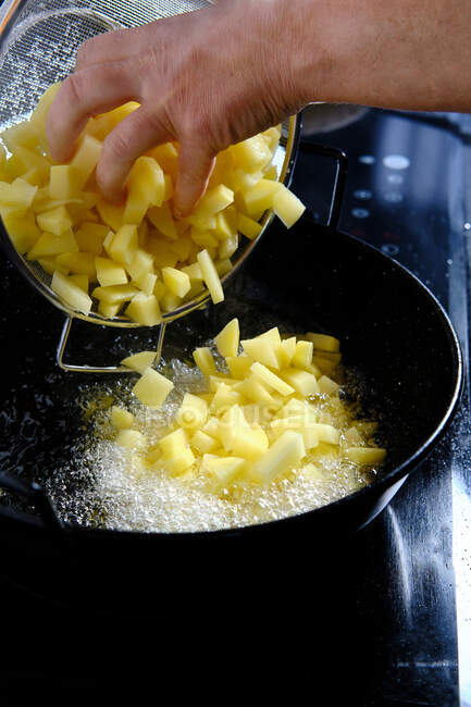 De arriba de la cosecha el cocinero vierte los trozos de las patatas del cedazo en la cacerola con el aceite que hierve en la cocina moderna - foto de stock