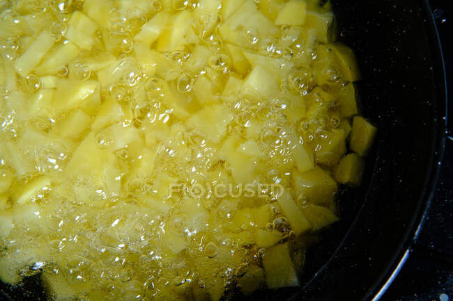 Top view of slices of yellow raw potatoes in big metal pan with boiling oil and bubbles in kitchen — Stock Photo
