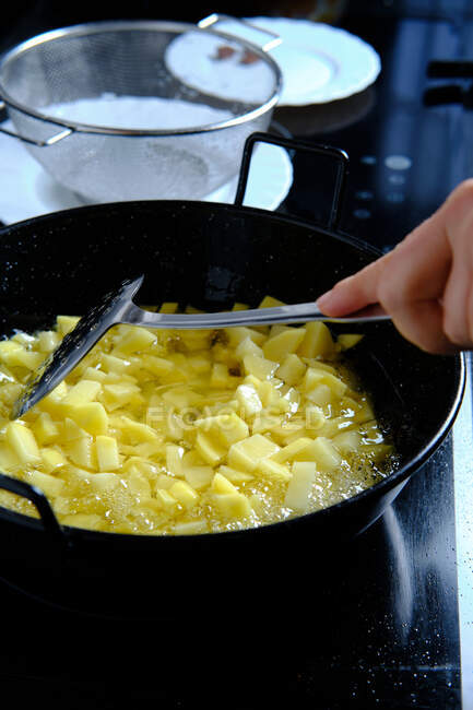 De arriba de la cosecha el cocinero vierte los trozos de las patatas del cedazo en la cacerola con el aceite que hierve en la cocina moderna - foto de stock