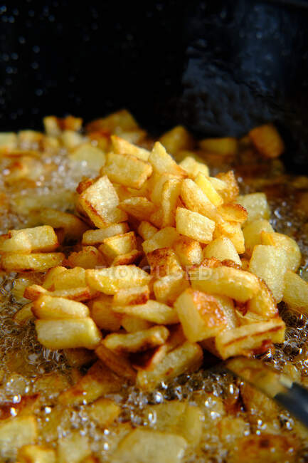 Vista superior de fatias de batatas cruas amarelas em grande panela de metal com óleo fervente e bolhas na cozinha — Fotografia de Stock