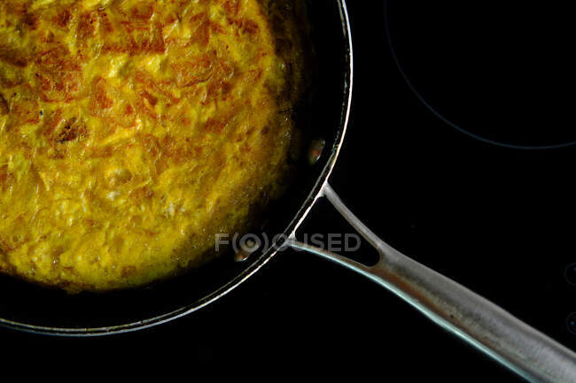 Зверху видніється металева сковорідка з смачним золотим іспанським омлетом, який смакує з оливковою олією на кухні. — стокове фото
