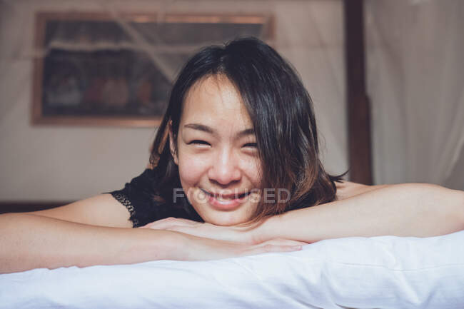 Optimiste asiatique femme regarder caméra couché sur confortable lit et rire tandis que couché sur lit le matin à la maison — Photo de stock