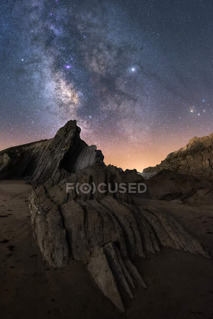 Von unten des rauen Klippengipfels unter der Milchstraße bunter blauer Nachthimmel und glänzende Sterne auf dem Hintergrund — Stockfoto