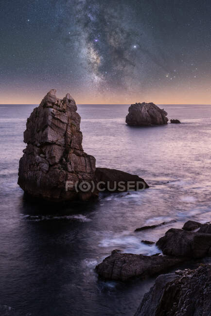 Große raue Klippen auf blauem, ruhigem Ozean am hellen Abend unter farbenfrohem Sternenhimmel mit Milchstraße — Stockfoto
