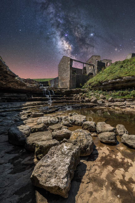 Знизу стародавнього кам'яного замку і невеликого водоспаду на сходах під темним небом з зірками і молочним способом — стокове фото