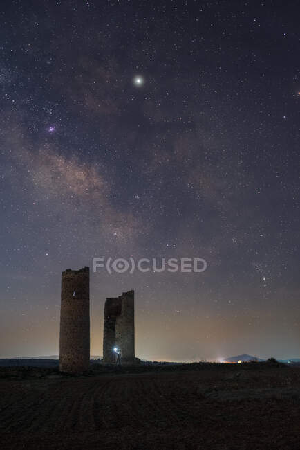 Anonymous person with lantern light on ancient stone towers on empty sandy ground under dark starry sky with milky way — Stock Photo