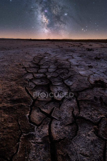 From above of dry cracked surface of ground and colorful night starry sky on horizon — Stock Photo