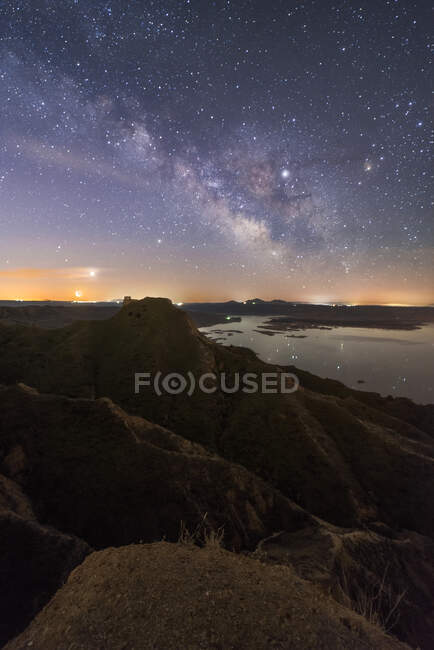 From above of tops of mountains and rocky valley with calm lake on background under colorful sky with milky way — Stock Photo