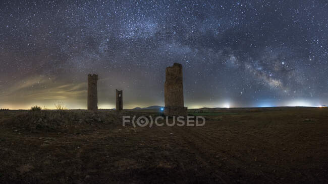Antiguas torres de piedra en tierra arenosa vacía bajo el cielo estrellado oscuro con la vía láctea - foto de stock