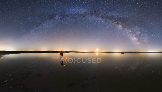 Silhouette eines anonymen Mannes, der auf der Reflexionsoberfläche des Wassers steht und den Sternenhimmel mit der Milchstraße erreicht — Stockfoto
