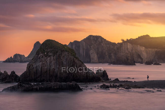 Pittoresca vista di maestosa scogliera sul mare calmo e la silhouette del viaggiatore durante il tramonto colorato — Foto stock