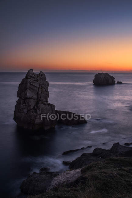 Desde arriba pintoresco paisaje de rocas ásperas entre el mar azul calma bajo el cielo de noche colorido con rayos de sol rompiendo a través de las nubes durante el crepúsculo Costa Brava, España - foto de stock