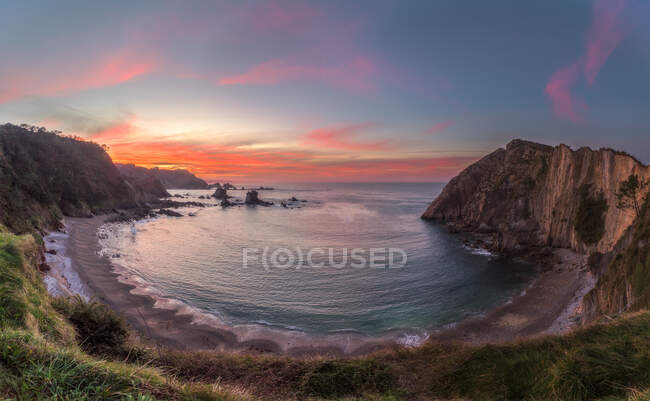 Lonely beach of calm lagoon among rough cliffs with colorful evening sky on background — Stock Photo