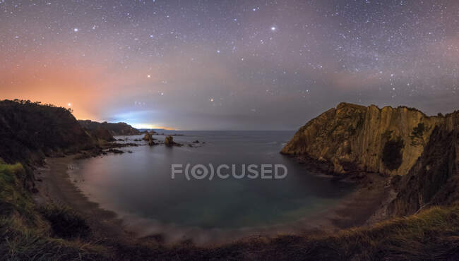 Playa solitaria de laguna tranquila entre acantilados ásperos con cielo nocturno colorido en el fondo - foto de stock