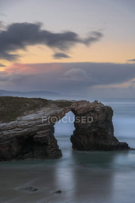 Grandi formazioni rocciose sulla spiaggia sabbiosa vuota dell'oceano con cielo serale nuvoloso e luminoso sullo sfondo — Foto stock