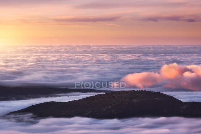 De cima de picos pretos de montanhas poderosas entre nuvens espessas brancas suaves ao nascer do sol — Fotografia de Stock