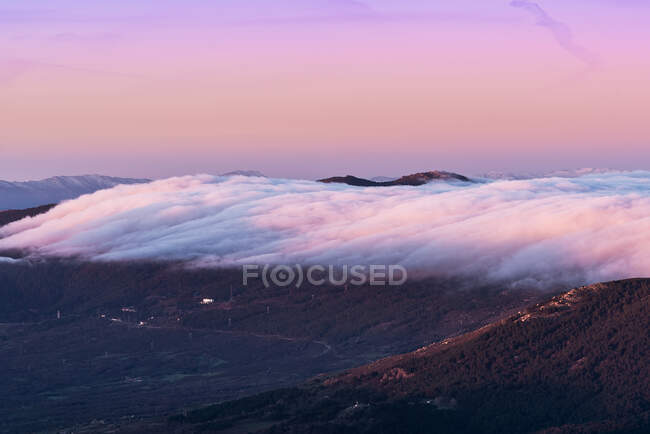 From above of old town on slope of hill among green forest covered with thick fog under colorful morning sky — Stock Photo