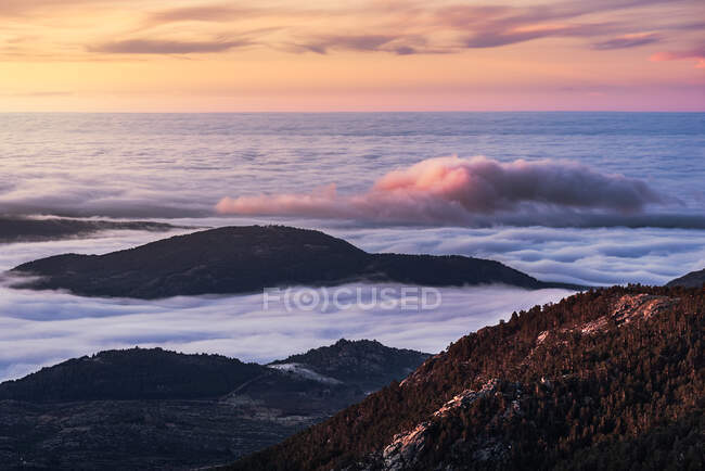 De arriba de los picos negros de las montañas potentes entre las nubes blancas suaves gordas al amanecer - foto de stock