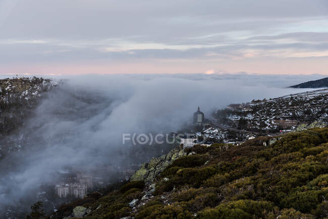 Dall'alto di centro storico su pendio di collina tra foresta verde coperta da nebbia densa sotto cielo colorato del mattino — Foto stock