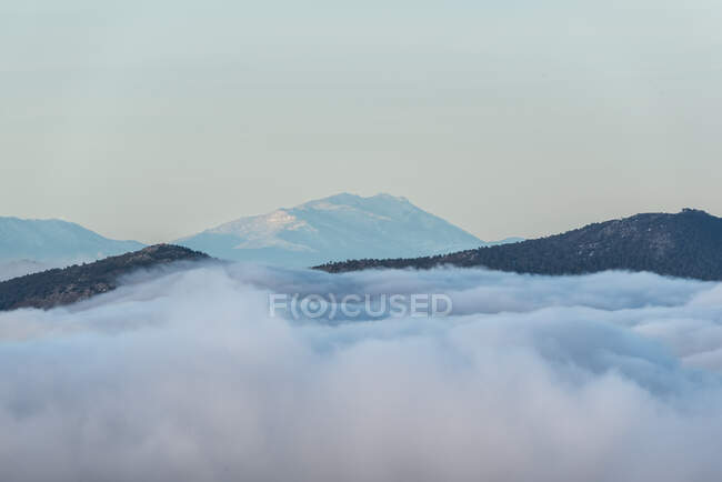 Dall'alto di cime nere di montagne potenti tra nubi spesse bianche morbide — Foto stock