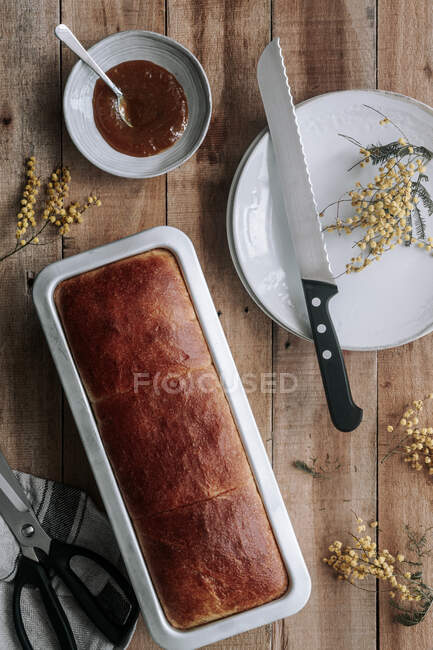 From above top view of rectangle loaf of fresh Brioche bread on wooden table with bowl of jam and knife — Stock Photo