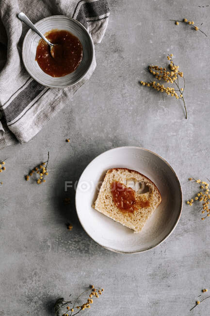Vue du dessus d'une tranche fraîche de pain Brioche enduite de confiture brune sur assiette avec cuillère sur table grise — Photo de stock