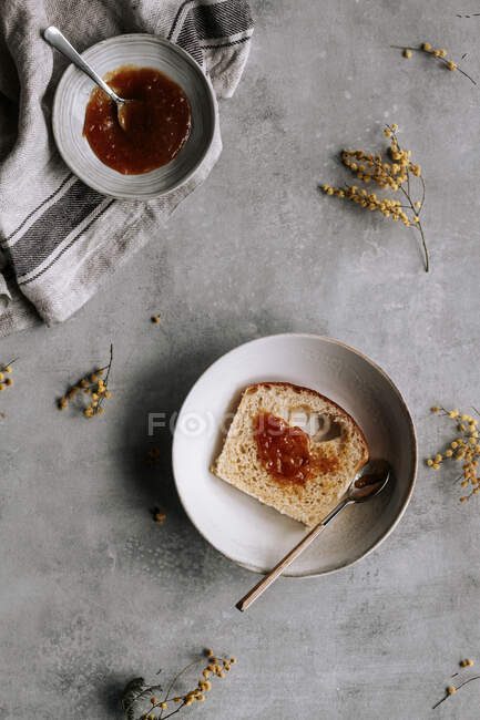 Top view of fresh slice of Brioche bread smeared with brown jam on plate with spoon on grey table — Stock Photo