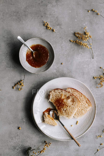 Вид сверху на свежий кусок хлеба Brioche, усеянный коричневым вареньем на тарелке с ложкой на сером столе — стоковое фото