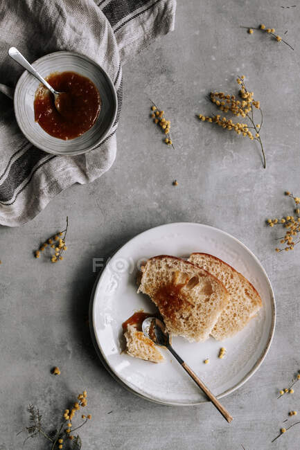 Vista superior de fatia fresca de pão Brioche manchado com geléia marrom na placa com colher na mesa cinza — Fotografia de Stock