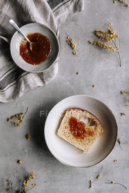 Vista superior de fatia fresca de pão Brioche manchado com geléia marrom na placa com colher na mesa cinza — Fotografia de Stock
