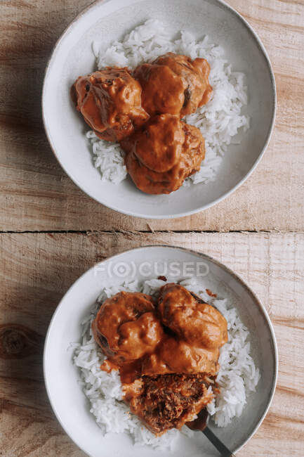 Vue du dessus des bols de riz et des délicieuses boulettes de lentilles avec sauce au curry placées près de l'épice et de la serviette sur une table en bois à la maison — Photo de stock