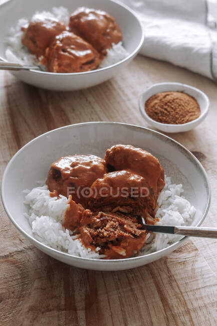 De arriba tazones de arroz y deliciosas albóndigas de lentejas con salsa de curry colocadas cerca de especias y servilletas en la mesa de madera en casa - foto de stock