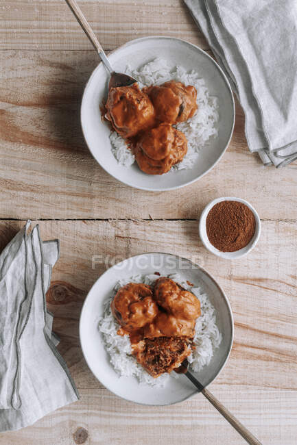 Vue du dessus des bols de riz et des délicieuses boulettes de lentilles avec sauce au curry placées près de l'épice et de la serviette sur une table en bois à la maison — Photo de stock