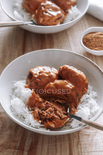From above bowls of rice and delicious lentil meatballs with curry sauce placed near spice and napkin on wooden table at home — Stock Photo