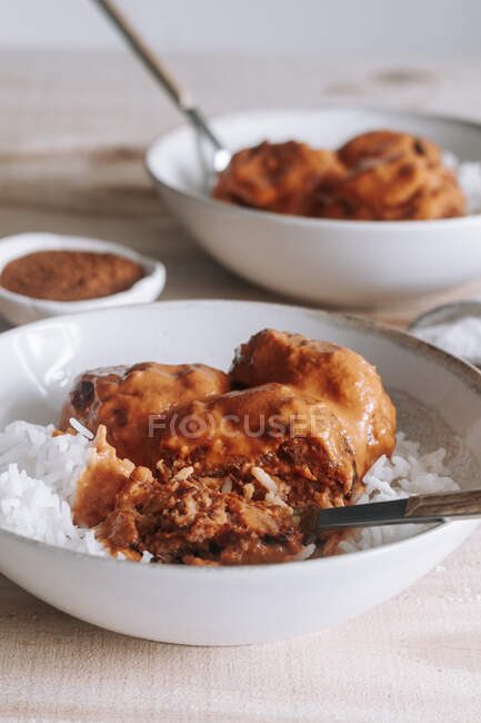 From above bowls of rice and delicious lentil meatballs with curry sauce placed near spice and napkin on wooden table at home — Stock Photo