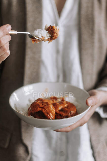 Unrecognizable female taking tasty curry lentil meatballs with rice with fork while eating during lunch at home — Stock Photo