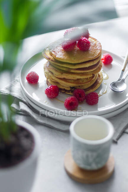 From above plate of delicious pancakes with raspberries placed on napkin near empty cup and potted plant in morning — Stock Photo