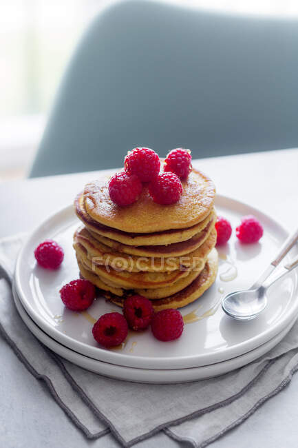 Stack of tasty pancakes with ripe raspberries placed on plate near spoons on gray background — Stock Photo