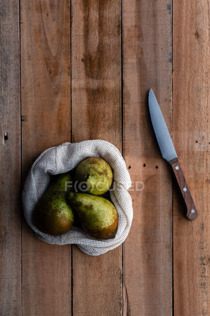 Верхний вид хлопкового мешка с сочными свежими грушами на деревянный стол с ножом — стоковое фото