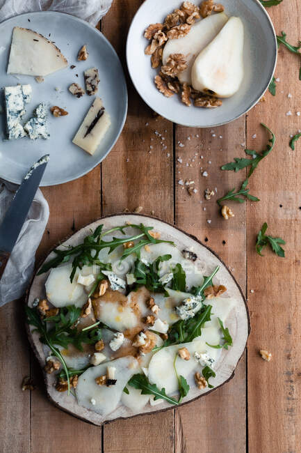 Vista superior da salada de pêra saborosa com rúcula colocada em madeira perto de queijo e nozes na cozinha — Fotografia de Stock