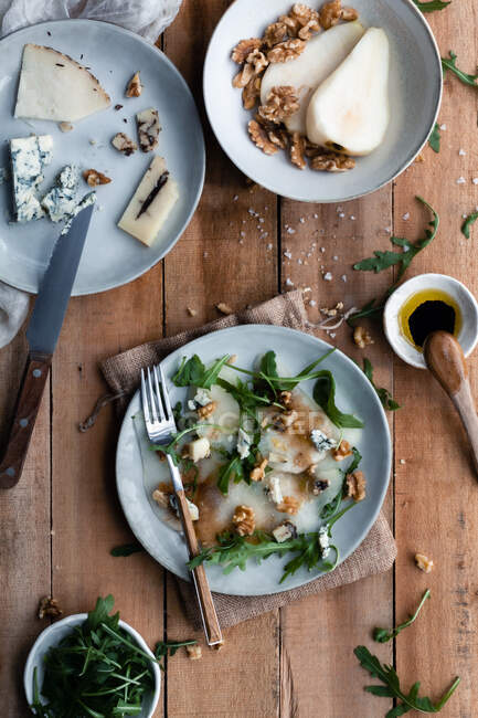 Вид зверху смачний грушевий салат з руколою, розміщений на деревині біля сиру та волоських горіхів на кухні — стокове фото