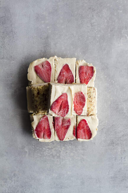 Draufsicht in Stücke geschnitten köstliche hausgemachte Frost Dessert mit weißer Sahne und Erdbeere in Scheiben geschnitten auf Marmor-Hintergrund — Stockfoto