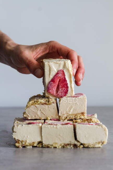 Pessoa de colheita segurando pedaço de sobremesa fria caseira apetitosa com creme branco e morango fresco sobre mesa de mármore — Fotografia de Stock