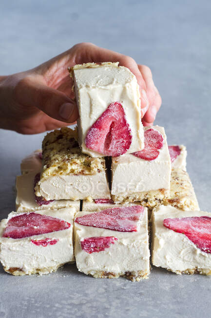 Crop persona in possesso di pezzo di appetitoso dessert freddo fatto in casa con panna bianca e fragola fresca sul tavolo di marmo — Foto stock